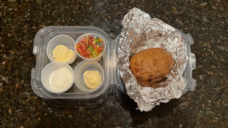 Takeout container with Outback Steakhouse baked potato and toppings on black table