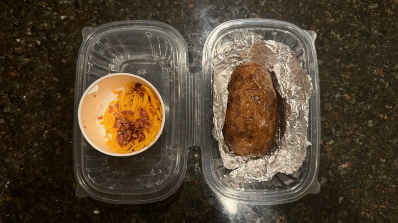 Takeout container with Texas Roadhouse baked potato and toppings on black table