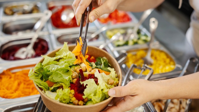A customer filling a bowl of salad on a buffet