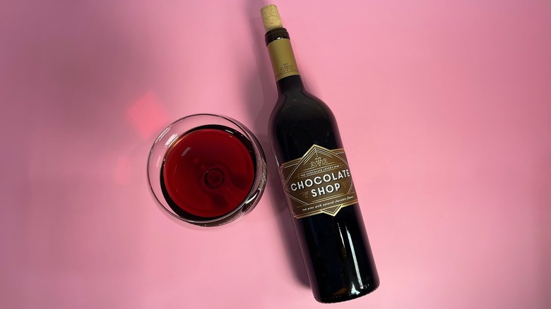 A bottle of Chocolate Shop next to a glass on a pink background
