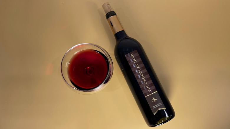 A bottle of Vin Chocolat Noir next to a glass on a tan background