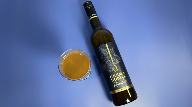 A bottle of Crema Nobile next to a glass on a blue background