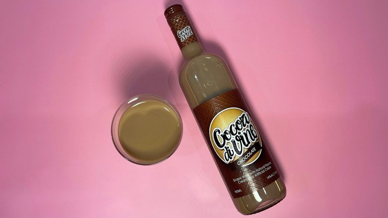 A bottle of Cocoa di Vine next to a glass on a pink background