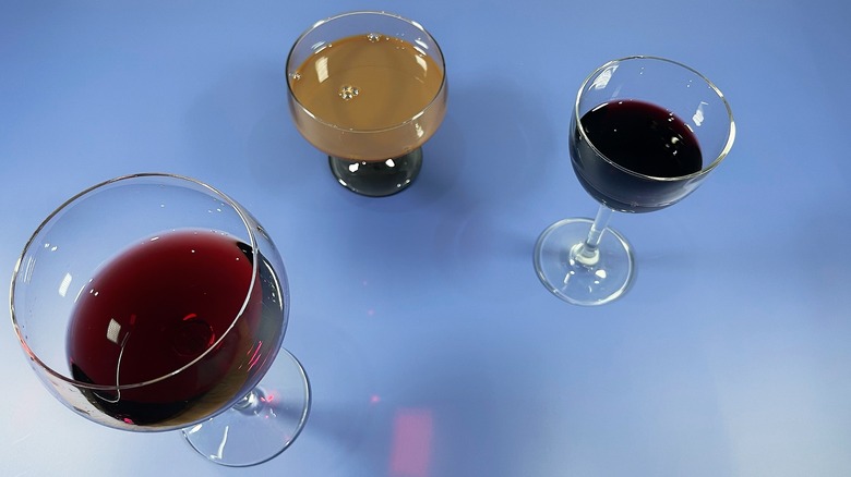 Three glasses of varying colors of chocolate wine arrange on a blue background