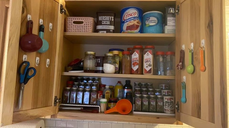 An open cabinet showing a spice rack with measuring cups and spoons hung on the inside of cabinet doors