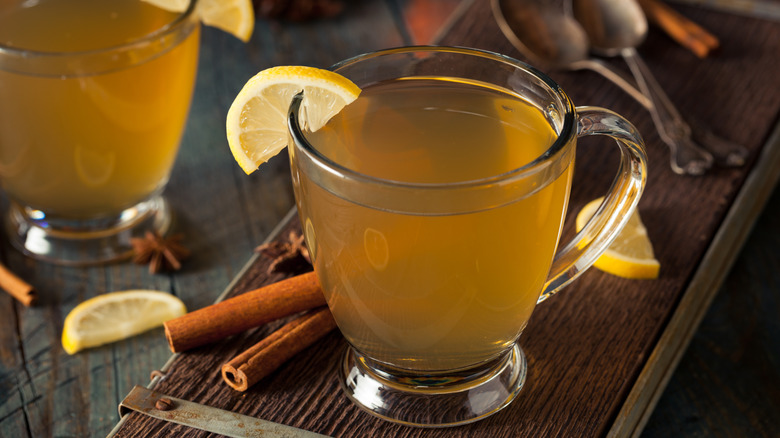A hot toddy in a clear glass on a thin wooden tray.