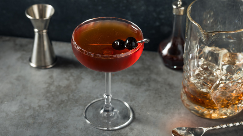 A Manhattan cocktail in a coupe beside an ice-filled pitcher for stirring.