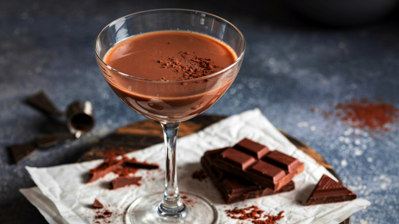 A chocolate martini is pictured with chocolate squares and cocoa powder on a tray.