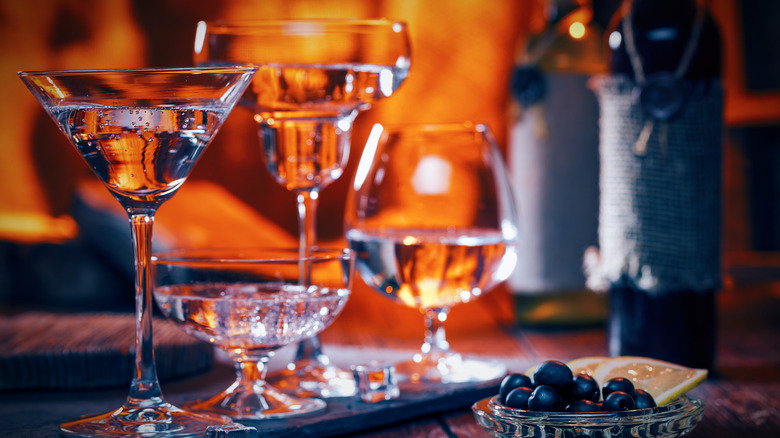 Several different cocktail glasses appear on a table in front of a roaring fire.