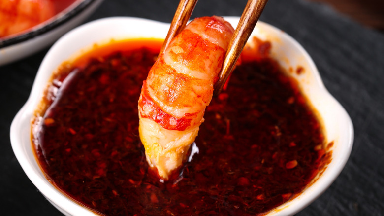 A crawfish tail being dipped in a red sauce by a pair of chopsticks