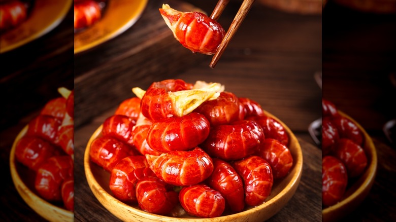 A bowl of crawfish tails and a set of chopsticks holding one tail