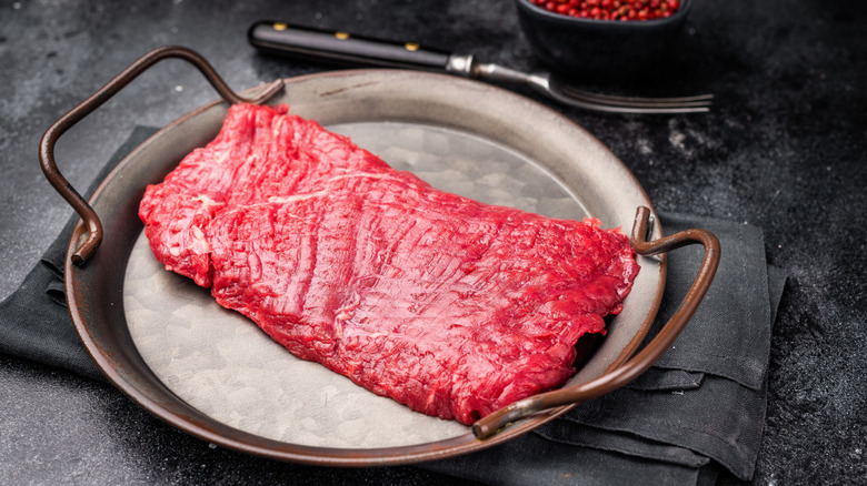 A raw flank steak on a metal tray.