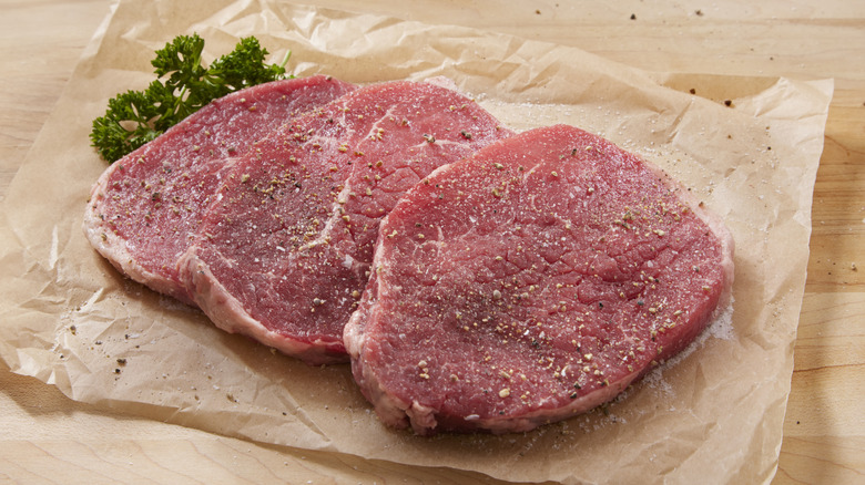 Two raw round steaks seasoned with salt and pepper on brown butcher paper.