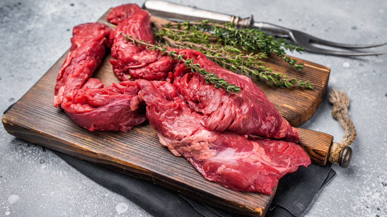 Raw skirt steak on a wooden cutting board with fresh herbs.
