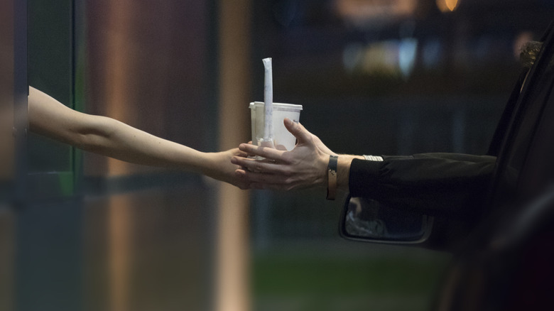 Fast food worker hands a drink to a customer in car at a drive-thru