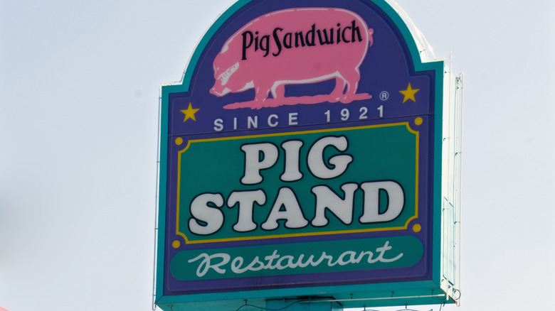 Sign for the Pig Stand, featuring a pink pig with "Pig Sandwich" written on its side on a blue background