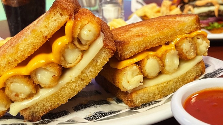 Two halves of a Denny's fried cheese melt sandwich shown closeup on a plate with a side dish of red sauce