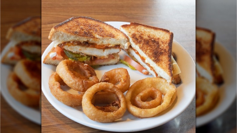 Denny's Nashville hot chicken melt, showing two halves of the sandwich diagonally cut, with onion rings on the side