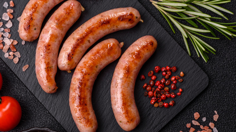 Cooked sausages arranged on slate with sprigs of rosemary, chunks of pink sea salt, and pink peppercorns.