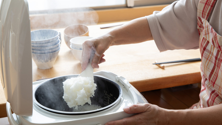 Person scooping out fresh, steaming rice from a rice cooker.