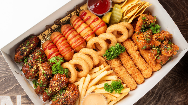 A box of fried foods, including corn dogs, wings, french fries, etc.