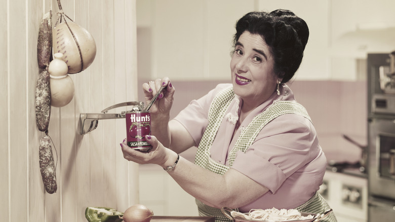 A photo of a woman opening a Hunt's can with a vintage wall-mounted can opener