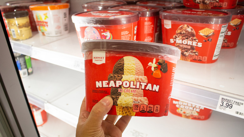 Hand holding a carton of Markey Pantry Neapolitan Ice Cream in front of freezer in Target