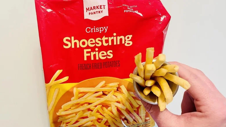 A bag of frozen Market Pantry Crispy Shoestring French Fries with a hand holding a small cooked cup of them