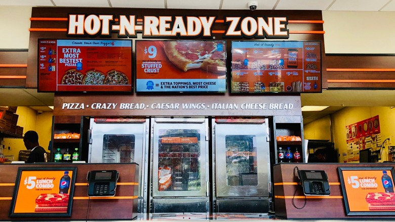 The counter of a Little Caesars store with a big illuminated sign for the Hot-N-Ready Zone