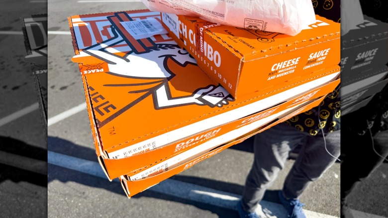 Close up shot of customer holding a stack of Little Caesars pizzas and lunch combo box