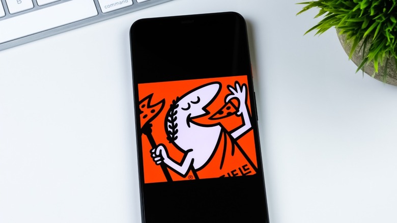 Little Caesars logo on phone screen laying on desk