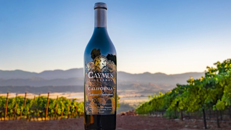 a bottle of Caymus Cabernet Sauvignon with a Napa Valley vineyard behind it