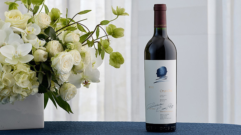 a bottle of 2022 Opus One red wine next to a vase of white flowers