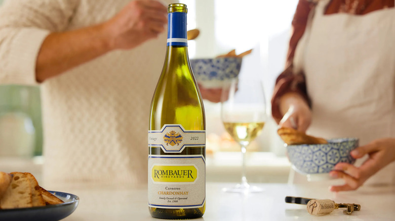 An opened bottle of Rombauer Chardonnay with two people snacking and drinking behind it