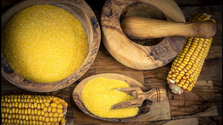 Cornmeal in wooden bowls and corn on the cob on a wooden background