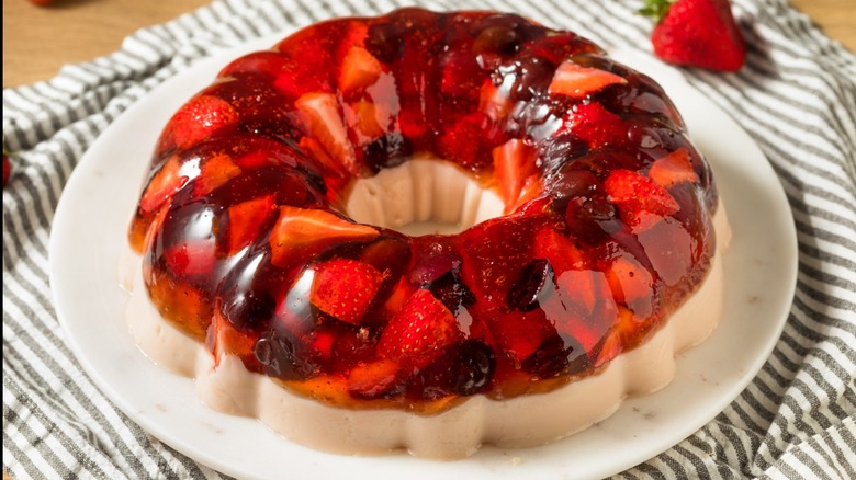 A gelatin mold with strawberries on a plate on top of a striped dishcloth