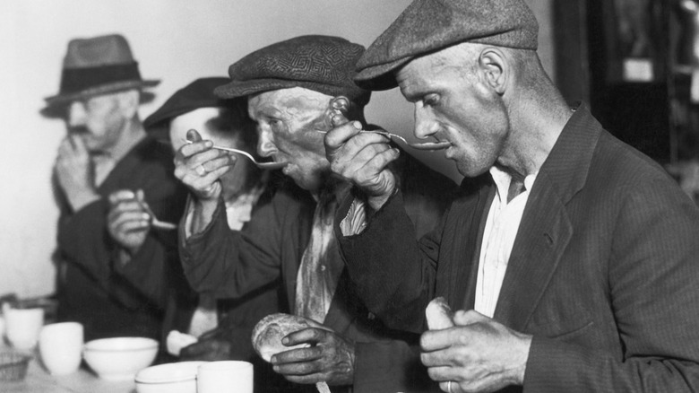 A black and white photo of men eating in a bread line during the Great Depression