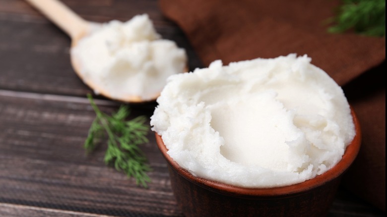 A bowl and spoon filled with lard with a wooden background with fresh herbs