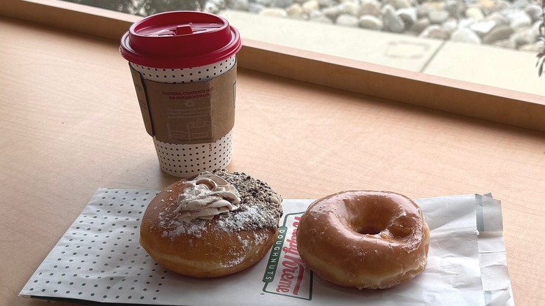 Two donuts next to a cup of coffee on a counter