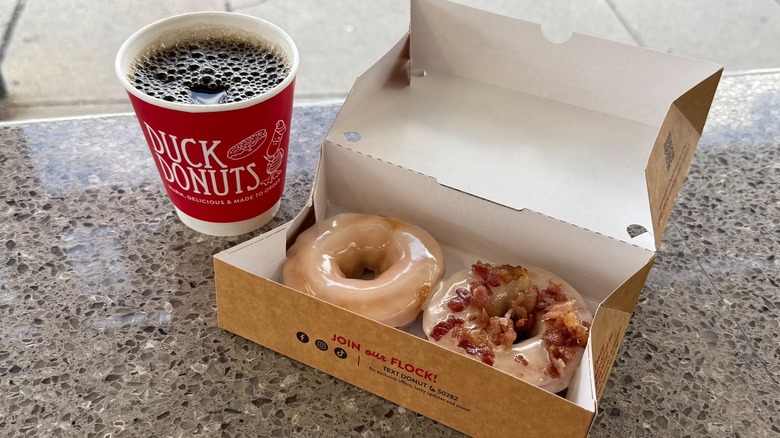 Two donuts in a to-go box next to a cup of coffee on a counter