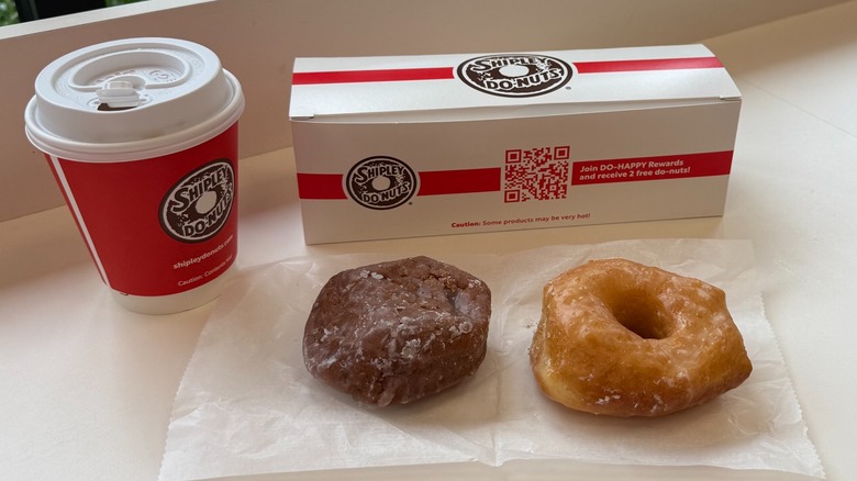 Two donuts next to a cup of coffee and box on a counter