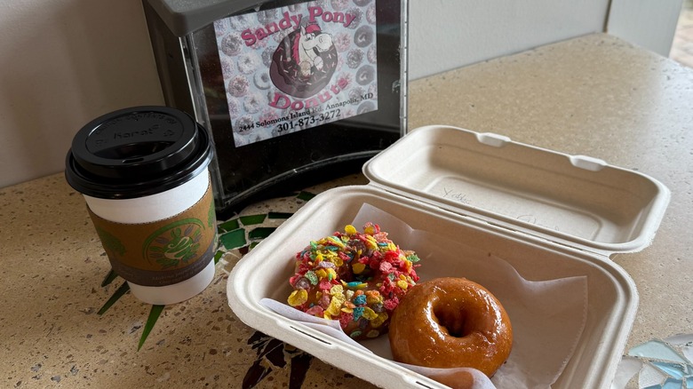 Two donuts in a to-go container next to a cup of coffee