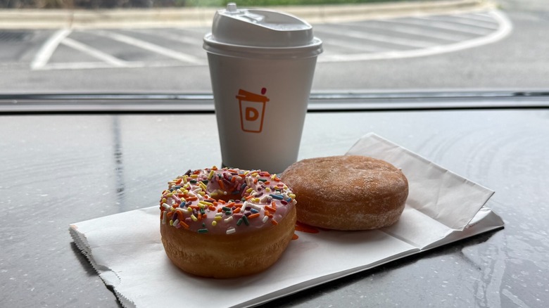 Two Dunkin donuts next to a cup of coffee on a counter
