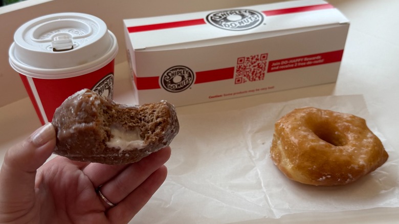 A woman holding a donut with a bite taken out next to another donut and a cup of coffee
