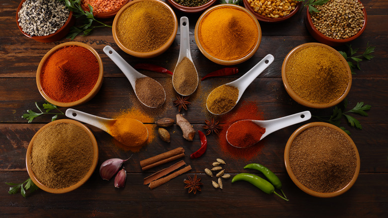 a variety of seasonings and spices in bowls and spoons on a wooden table