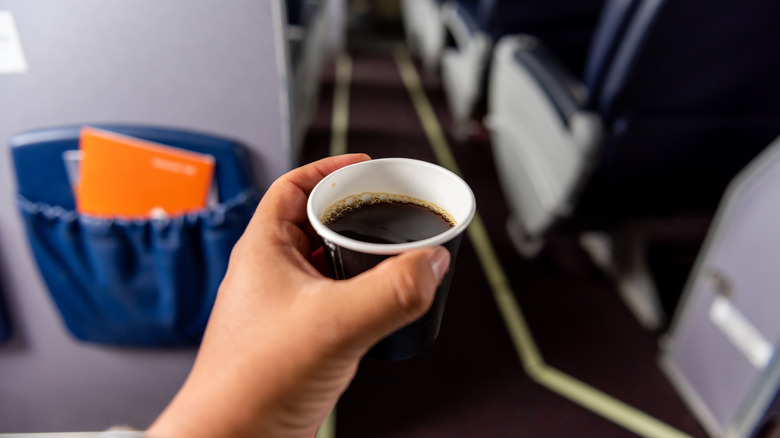 A hand holding an in-flight coffee cup
