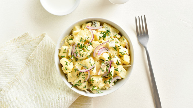 Bowl of potato salad with herbs and onions, a fork and napkin on the side