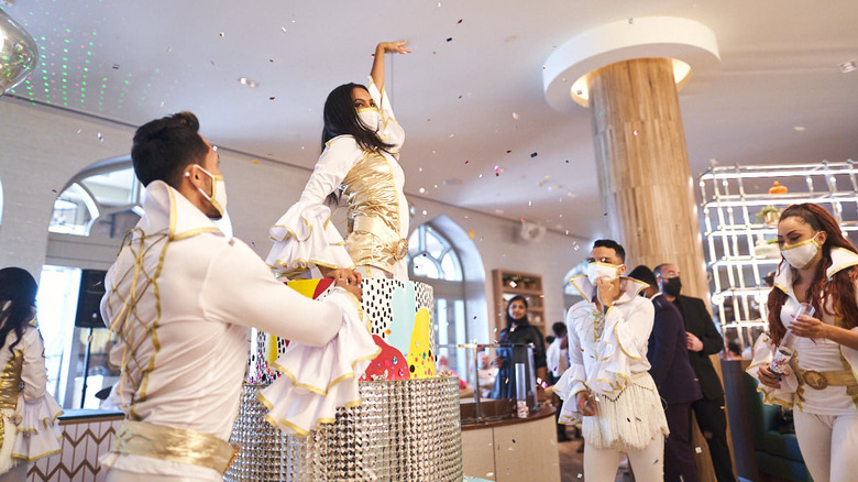 A woman popping out of a fake cake with confetti at brunch party