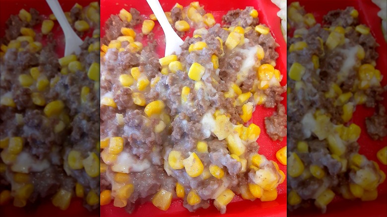 Close-up of a red plastic lunch tray with mashed potatoes covered in a creamy mixture of beef gravy and corn