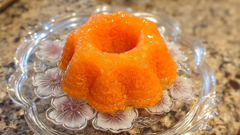 A small mold of lemon Jell-O carrot salad on a decorative glass platter
